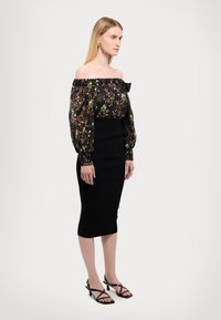 Μαύρη ανθισμένη μπλούζα με ανοιχτούς ώμους και διάφανα μακριά μανίκια, συνδυασμένη με μια εφαρμοστή μαύρη μολυβένια φούστα και μαύρες πέδιλες με λουράκια.