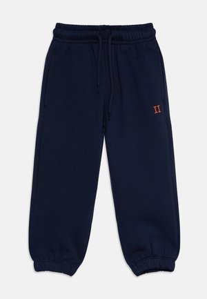 Pantalon de survêtement bleu marine avec taille élastique, chevilles resserrées et cordon, avec un petit chiffre romain II orange sur la cuisse gauche.