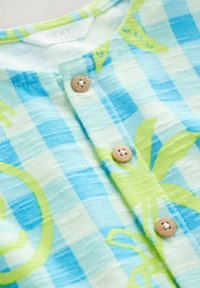 Chemise à carreaux bleu clair et blanc avec des imprimés de palmiers verts et des boutons beige sur la patte de boutonnage avant.