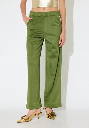 Grüne weite Hosen aus glattem Stoff, mit Seitentaschen und einem taillierten Bund, kombiniert mit goldenen Slingback-Absätzen mit einer Schleifendetail.