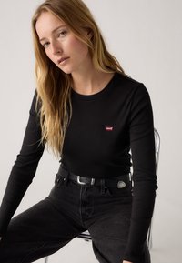 Černé tričko s dlouhým rukávem a malým červeným logem Levi's. Nošeno s černými džínami a černým pásem se stříbrnou sponou. Jednoduchý design, přiléhavý střih.