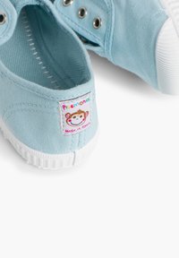 Heledad sinine kangastossud valge kummitald ja aukudega. Omab värvilist kangasildiga, millel on naeratav ahv ja tekst "Pisamonas".