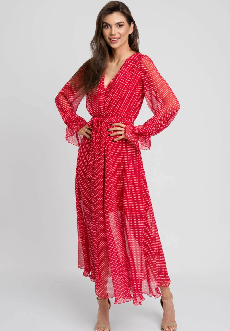 Czerwona maxi sukienka w kropki z lekkiego szyfonu, z długimi przezroczystymi rękawami, zapinana w stylu na wiastek i z przewiązanym w pasie, co pozwala na regulację dopasowania.