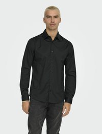 Zwarte langemouwen shirt gemaakt van soepele stof, met een button-down kraag, knopen aan de voorkant en een getailleerd ontwerp. Gemaakt met donkere jeans.