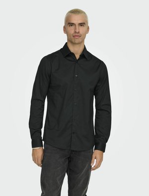 Zwarte langemouwen shirt gemaakt van soepele stof, met een button-down kraag, knopen aan de voorkant en een getailleerd ontwerp. Gemaakt met donkere jeans.