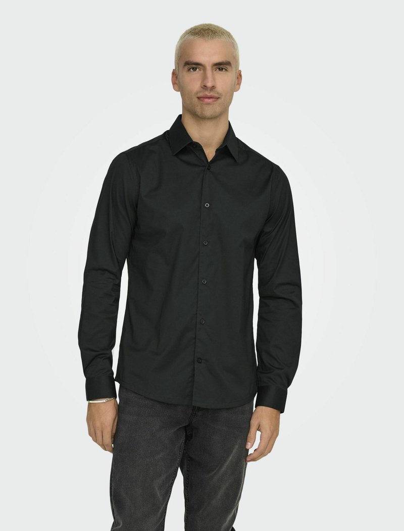 Zwarte langemouwen shirt gemaakt van soepele stof, met een button-down kraag, knopen aan de voorkant en een getailleerd ontwerp. Gemaakt met donkere jeans.