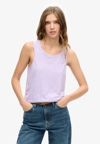 Lichtpaarse mouwloze tanktop van zacht materiaal, met een ronde halslijn en een klein logodetail aan de voorkant. Draagt met hoge taille spijkerbroek.