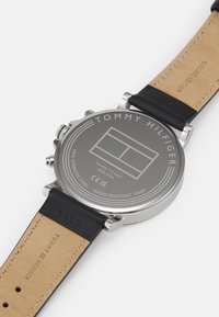 Fond de montre en acier inoxydable avec logo gravé, étanche jusqu'à 5 bars, avec un bracelet en cuir noir et une face beige.