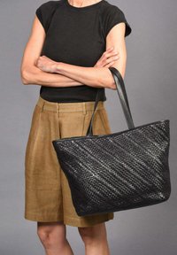 Bolso tote tejido negro con patrón diagonal, que cuenta con dos asas de cuero negro. El bolso tiene una forma estructurada y una textura suave.