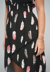 Czarna sukienka z marszczoną talią i asymetrycznym dołem. Ozdobiona wzorami różowych i szarych piór na lekkiej tkaninie.