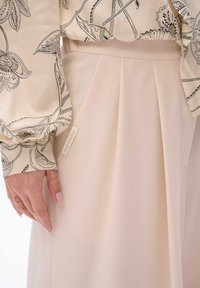 Beige plooienrok van lichtgewicht stof, gecombineerd met een gebloemd blouse met zwarte botanische ontwerpen en een label met de tekst "blue shadow."