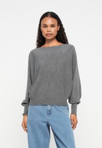 Pullover cinza leve com um amplo decote, corte solto e mangas longas. Combinado com jeans de denim azul claro.