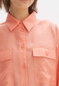 Koraal kleurige button-up shirt met een kraag, twee borstzakken en een licht gekreukt textuur. Beschikt over bijpassende knopen en een relaxte pasvorm.