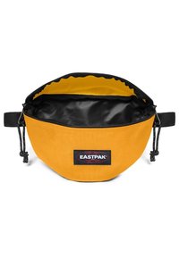 Banane Eastpak jaune avec fermeture éclair noire et intérieur noir, ouverture sur le dessus et sangle noire réglable sur fond blanc.