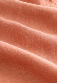 Perzikgekleurde linnen stof met een textured oppervlakte, gekenmerkt door zachte plooien en een subtiel geweven patroon. Glad en lichtgewicht uiterlijk.