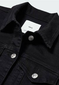Veste en jean noire avec boutons-pression argentés, col pointu, poche poitrine à rabat et étiquette de marque blanche visible à l'intérieur du col.