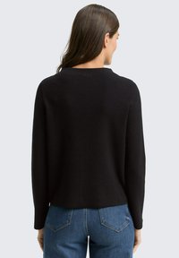 Zwart gebreid sweater met een ronde halslijn, lange mouwen en een relaxed fit; gecombineerd met blauwe denim jeans met achterzakken.