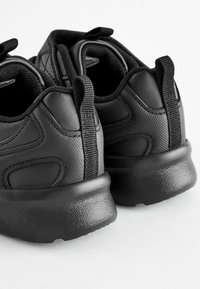 Chaussures de sport noires avec une semelle en caoutchouc texturé, un intérieur rembourré, un dessus en tissu et cuir, et des languettes à l'arrière pour un enfilage facile.
