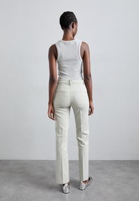 Lichtgroene op maat gemaakte broek met een slim fit en achterzakken, gecombineerd met een grijze mouwloze top. Gladde textuur en subtiele stikdetails.
