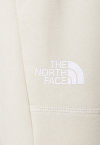 Crèmewitte stof met een gestructureerde afwerking. Het logo "THE NORTH FACE" is prominent in het wit weergegeven op het onderste gedeelte.