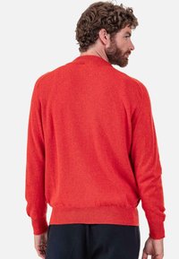 Roter Strickpullover mit langen Ärmeln, gerippten Bündchen und Saum sowie lockerem Sitz. Das Material wirkt weich und strukturiert mit einem leichten Glanz.