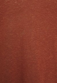 Rustinvärinen kangas, jossa on hieno, hieman teksturoitu kudos; vaikuttaa kevyeltä ja pehmeältä, ja siinä on hienovaraisia sävyeroja.