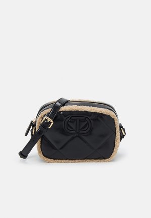 Zwarte gewatteerde schoudertas met beige schapenvachtaccent, frontaal geperst logo, gouden gesp en verstelbare riem op effen achtergrond.