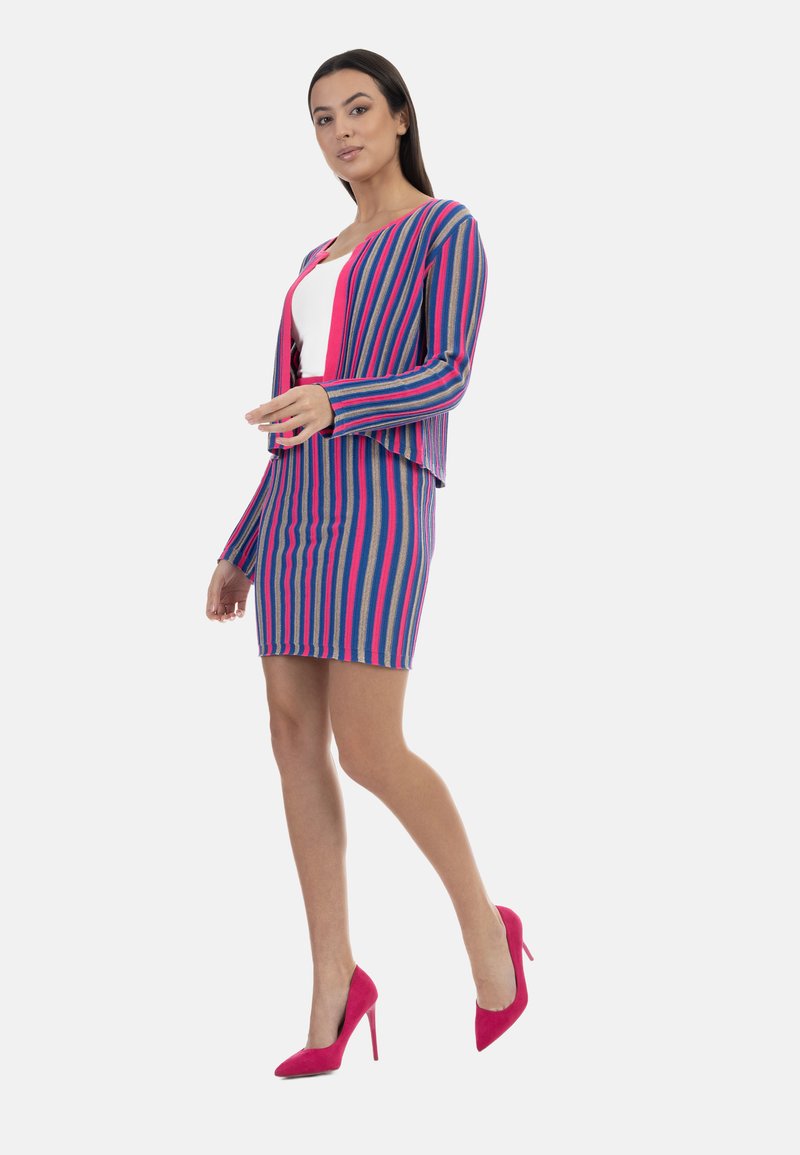 Mångfärgad randig klädsel med en figursydd kjol och en matchande kort cardigan. Färgerna inkluderar blå, rosa och beige. Ett par rosa klackar.