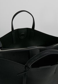 Czarna skórzana torba typu tote z teksturowanym wykończeniem, z zamkiem błyskawicznym, dwoma uchwytami i pojemnym, niepodszewkowanym wnętrzem.