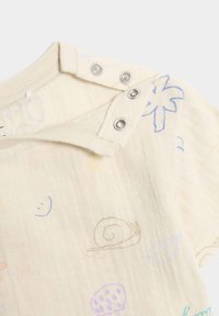 Un body en coton bio de couleur beige clair avec des motifs pastel imprimés d'escargots, de champignons et de visages souriants ; doté de boutons pression au niveau du col.