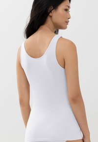 White, fitted tank top made of smooth, stretchy fabric. Features a scoop neckline and medium-width straps. No visible patterns or hardware.