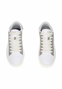 Un paio di sneakers bianche con pannelli laterali grigi e lacci bianchi, viste dall'alto, con il marchio "GAP" sulla linguetta.