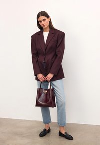 Burgundy kavaj med strukturerade axlar, vit skjorta, ljusblå jeans, svarta loafers och en glänsande väska i krokodilmönster.