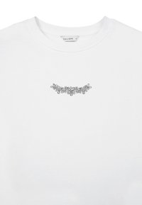 T-shirt en coton blanc avec un embellissement floral argenté au centre devant, un col rond et des manches courtes.