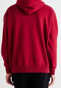 Rode hoodie met een ontspannen pasvorm, zachte textuur, ribgebreide boorden en zoom, en zonder zichtbare logo's of patronen.