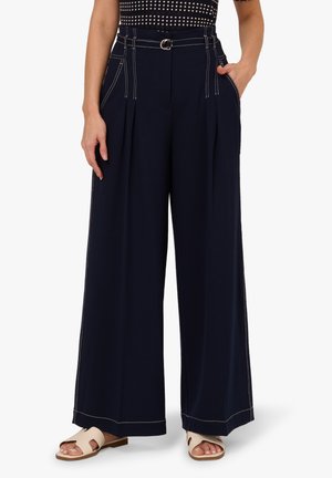 Marineblaue Hosen mit weitem Bein und Bügelfalten, mit kontrastierenden weißen Nähten, einem Gürtel mit Metallverschluss und seitlichen Taschen.
