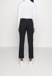 Svarta byxor med rak passform, utrustade med två bakfickor och knäppning. Bärs med en vit långärmad topp och vita sneakers.