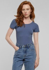 Modra kratka bodi majica z rokavi, izdelana iz mehkih materialov, v kombinaciji z visokim pasom svetlim džinsom, ki ima zavezovanje na gumbe in žepke.