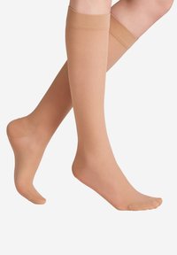 Bézs színű térdig érő harisnya sima felülettel, megerősített orrésszel, valamint puha, rugalmas szegéllyel a kényelem érdekében.