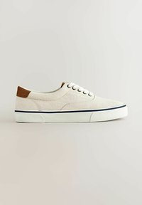 Baskets basses en toile beige avec lacets blancs, patch marron au talon, semelle en caoutchouc blanche avec une bande bleu marine, vue de côté.