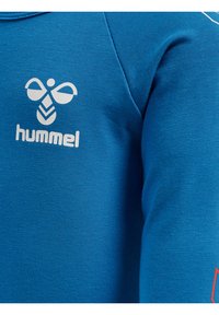 Blauer Baumwoll-Sweatshirt mit langen Ärmeln, ausgestattet mit einem weißen Logo und Branding auf der Brust. Glatte Textur mit figurbetontem Schnitt.