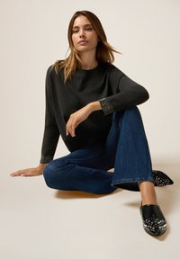 Svart tröja med texturerade ärmar, tillsammans med utsvängda blå jeans. Svarta skor med spetsig tå prydda med silvernitar fulländar outfiten.