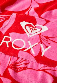 Tejido de la marca Roxy en rojo y rosa con patrones florales. La superficie texturizada presenta un logo blanco, un corazón y letras en negrita.