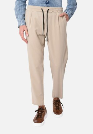 Pantaloni beige con coulisse indossati con una camicia di jeans blu, con tasche laterali e sneakers alte in pelle marrone con suola bianca.