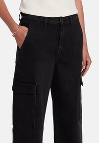 Pantaloni cargo in denim nero con tasche laterali, vestibilità rilassata e texture liscia; presenta una chiusura con bottone e zip in vita.