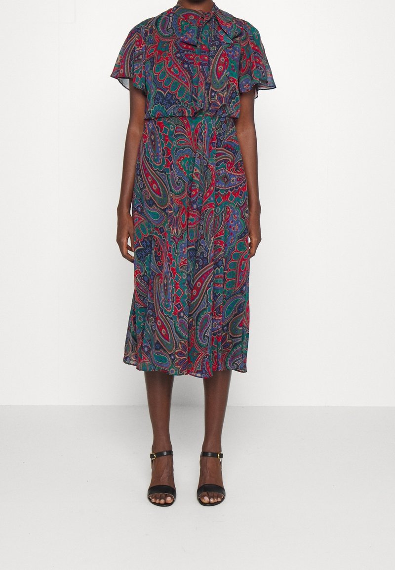 Blommig paisleymönstrad klänning med krage och knappar, korta ärmar och en A-linjeformad kjol. Har ett knytbälte och färgstarka detaljer.
