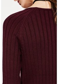 Burgundy ribbed knit neule, jossa on pystysuuntaiset viivat, pyöreä pääntie ja hillitty tekstuuri. Ei näkyviä kuvioita tai metalliosia.