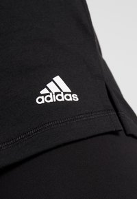 Top sportivo nero con scollatura rotonda e piccolo logo Adidas bianco sul lato sinistro. Il tessuto è morbido e elastico.