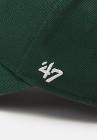 Green cap featuring textured fabric, curved brim, and a white embroidered logo positioned on the side.