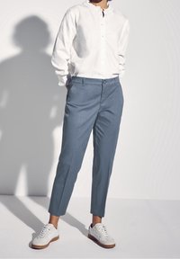 Camicetta bianca leggera con colletto arricciato, abbinata a pantaloni blue slim-fit alla caviglia e sneakers bianche con suola marrone.